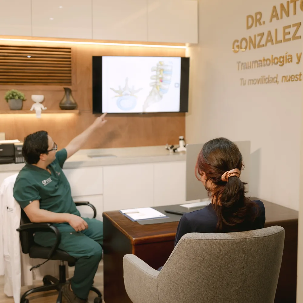 El Dr. González Tovar explicándole una lesión de columna a una paciente en la pantalla de su consultorio.